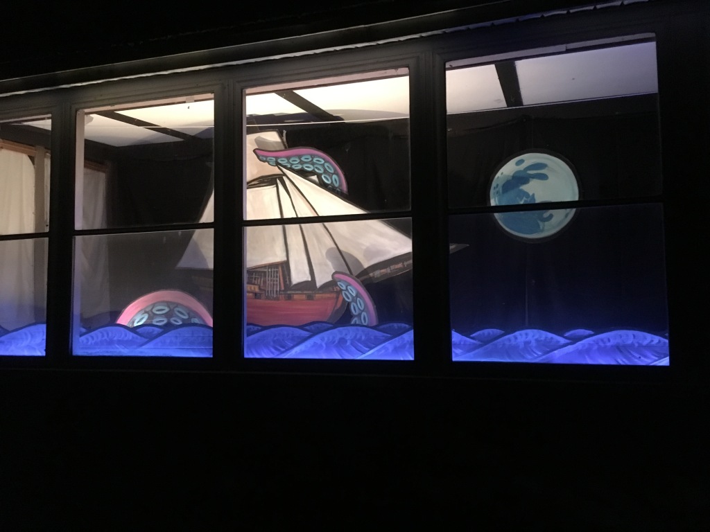 porch window with the full moon rising over the sea, a pirate ship, and three tentacles rising up over the side of the ship.